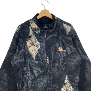 May include: A black fleece jacket with a camouflage pattern and the Mossy Oak logo. The jacket has a zipper closure and a stand-up collar.