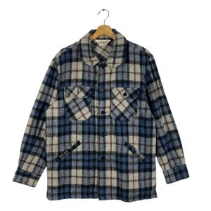 May include: A blue, beige, and brown plaid button-up shirt with two chest pockets and two side pockets. The shirt has a collar and is hanging on a wooden hanger. The brand name "RENDOCK" is visible on the collar.