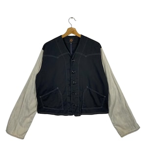 Puede incluir: Una chaqueta vaquera negra con cierre de botones y dos bolsillos. Las mangas están hechas de una tela de color claro.