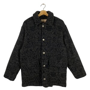 May include: A grey patterned wool jacket with a button closure and two large pockets. The jacket has a collar and is hanging on a wooden hanger.
