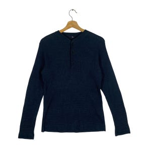 May include: Dark navy blue long-sleeve Henley shirt with a textured waffle knit design. The shirt features a three-button placket and a classic collar. The shirt is hanging on a wooden hanger.