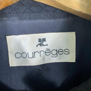 Puede incluir: Una etiqueta blanca con texto negro que dice "Courr&egrave;ges" con un logotipo "C" estilizado sobre el texto.