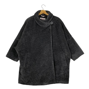 May include: A dark gray, oversized coat with a unique asymmetrical design. The coat features a large collar, a single button closure, and three-quarter length sleeves. The coat is made of a soft, textured material and hangs on a wooden hanger.