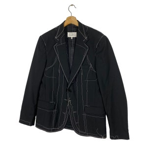 May include: A black blazer with white stitching detail. The blazer has a single button closure and two pockets. The label reads "Maison Margiela" in white text.