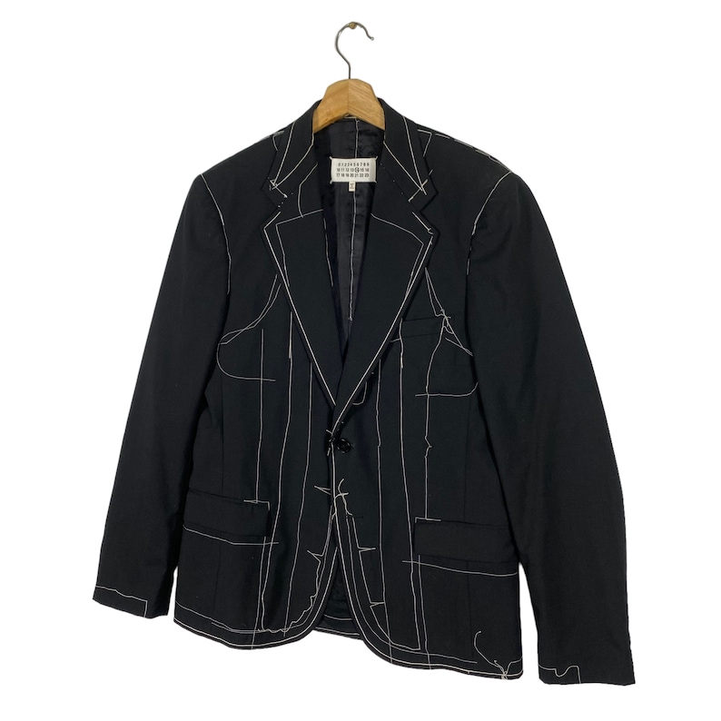 May include: A black blazer with white stitching detail. The blazer has a single button closure and two pockets. The label reads "Maison Margiela" in white text.