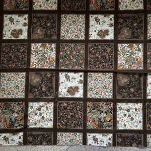 May include: A brown fabric with a repeating pattern of squares. Each square has a different floral design in shades of brown, white, and pink.