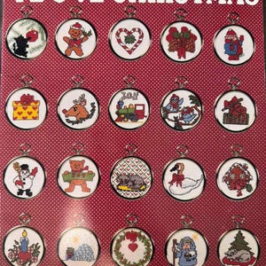 May include: A red and white polka dot pattern book cover titled I LOVE CHRISTMAS, Book 408, featuring twenty circular cross-stitch ornaments. Designs include a gingerbread person, candy cane heart, train, snowman, swan, and various holiday motifs.