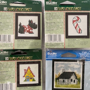May include: Four Bucilla counted cross stitch kits featuring designs by Mary Engelbreit. The kits include a Scottish Terrier, a candy cane, a small house, and a Western-style house. Each kit includes Aida cloth, floss, needle, and instructions.