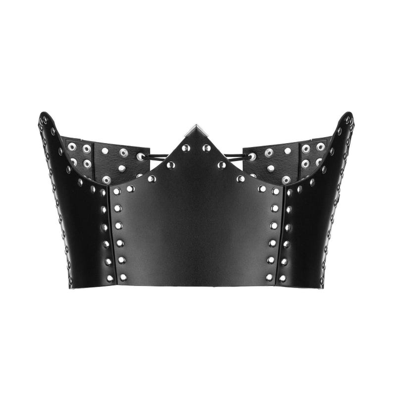 May include: A black leather crown with a pointed center and curved sides. The crown is adorned with silver-colored grommets along the edges and around the top, creating a bold and edgy aesthetic. The design is symmetrical and stands out against the white background.