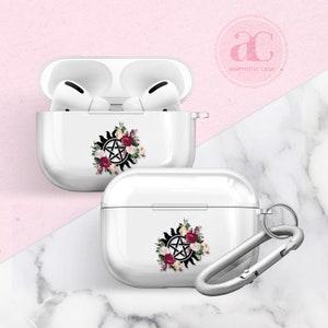 Puede incluir: Funda blanca para Airpods con un diseño floral que incluye un pentagrama negro y un símbolo solar. La funda tiene un mosquetón plateado.