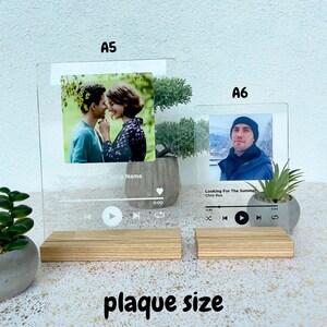 May include: Two clear acrylic music player plaques with a photo and song title. The larger plaque is labelled "A5" and the smaller plaque is labelled "A6". Both plaques have a wooden base.