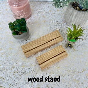 May include: Two wooden display stands with a groove in the centre. The stands are made of light brown wood and are sitting on a white surface with gold flecks. The text "wood stand" is written below the stands.