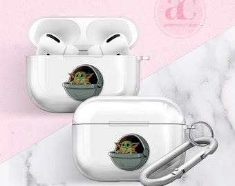 May include: White protective case for AirPods featuring a cartoon image of a green alien character from the Star Wars franchise. The case has a silver carabiner clip attached.
