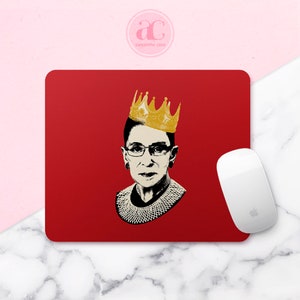 May include: Red mouse pad with a black and white image of Ruth Bader Ginsburg wearing a gold crown.