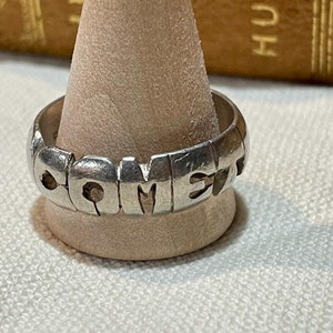 May include: A silver ring with the word "COMET" spelled out in raised letters.