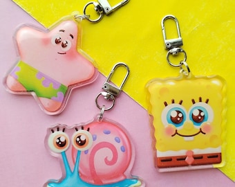 May include: Three cartoon character keychains: a pink starfish with green shorts, a pink snail with a blue shell, and a yellow sponge with a brown tie. Each keychain has a silver clasp for attaching to keys or bags.