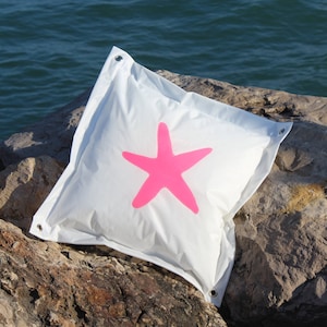 May include: White beanbag chair with a pink starfish design. The beanbag is sitting on a rocky surface.
