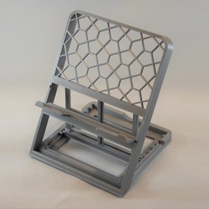 May include: A gray 3D printed phone stand with a honeycomb pattern on the back. The stand is designed to hold a phone upright.