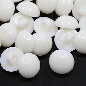 May include: A collection of white plastic buttons with a dome shape and a small loop on the back.
