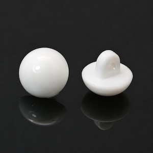 May include: Two smooth, glossy white spherical buttons. One button is shown from the front, displaying a perfectly round, solid white surface. The second button is positioned to show its flat base and the small, protruding shank with a hole.