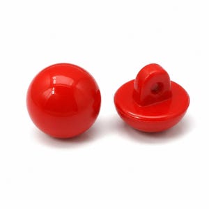 May include: Two bright red spherical buttons with a smooth, glossy finish. One button is positioned to show its rounded top surface, while the other is turned to reveal the flat base and the integrated loop shank with a hole for attachment.