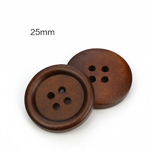 Könnte beinhalten: Zwei dunkelbraune Holzknöpfe mit jeweils vier Löchern zum Annähen. Die Knöpfe sind rund und haben einen Durchmesser von 2,5 cm. Der Text "25mm" ist sichtbar. Geeignet für verschiedene Nähprojekte.