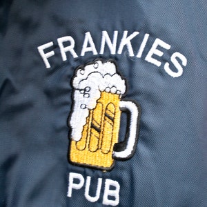 May include: A blue embroidered patch with the text "FRANKIES PUB" and a cartoon image of a beer mug with foam on top.