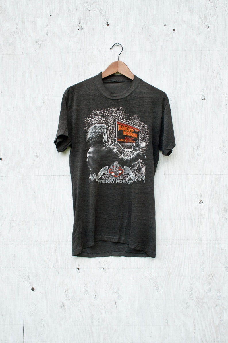 May include: A dark gray t-shirt with a graphic print of a person riding a Harley Davidson motorcycle. The graphic includes the text "Harley Davidson" and "Follow Nobody".