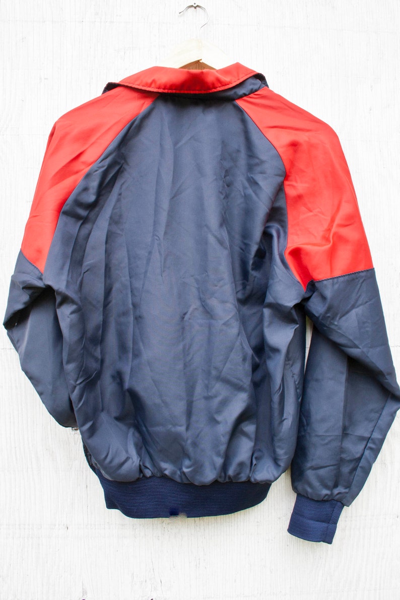 May include: A navy blue and red windbreaker jacket with a zipper closure. The jacket has a stand-up collar and long sleeves.