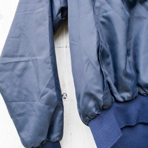 May include: A blue and red windbreaker jacket with a white stripe around the collar and cuffs. The jacket has a zipper closure and a ribbed waistband.