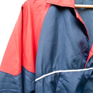 May include: A blue and red windbreaker jacket with a white stripe around the bottom. The jacket has a zipper closure and a collar.