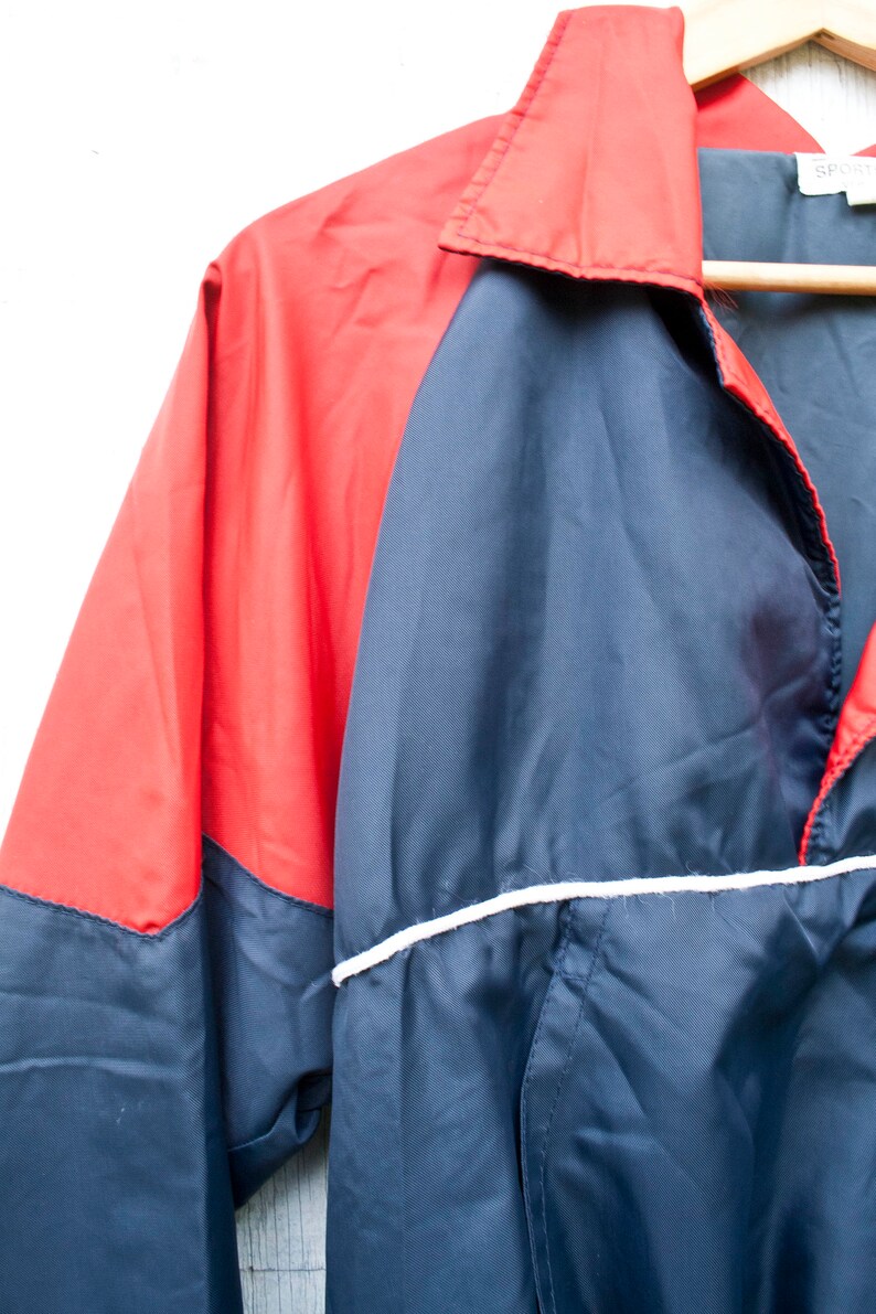 May include: A blue and red windbreaker jacket with a white stripe around the bottom. The jacket has a zipper closure and a collar.