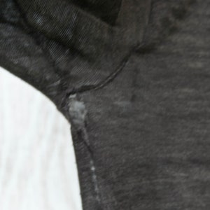 May include: Close-up of a dark gray fabric with a slight texture. The fabric has a small tear near the seam.