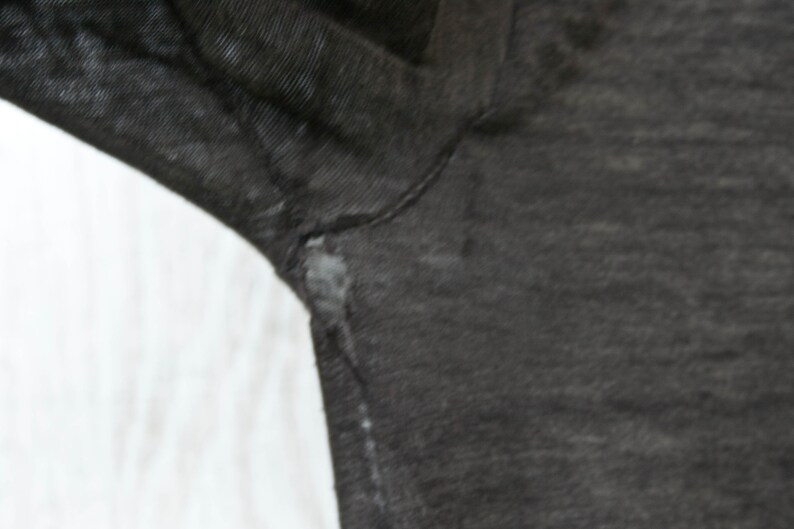 May include: Close-up of a dark gray fabric with a slight texture. The fabric has a small tear near the seam.