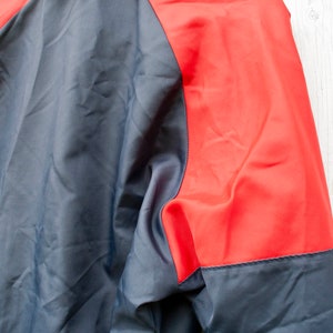 May include: A navy blue and red jacket with a zipper closure. The jacket has a red panel on the right side of the back and sleeves.