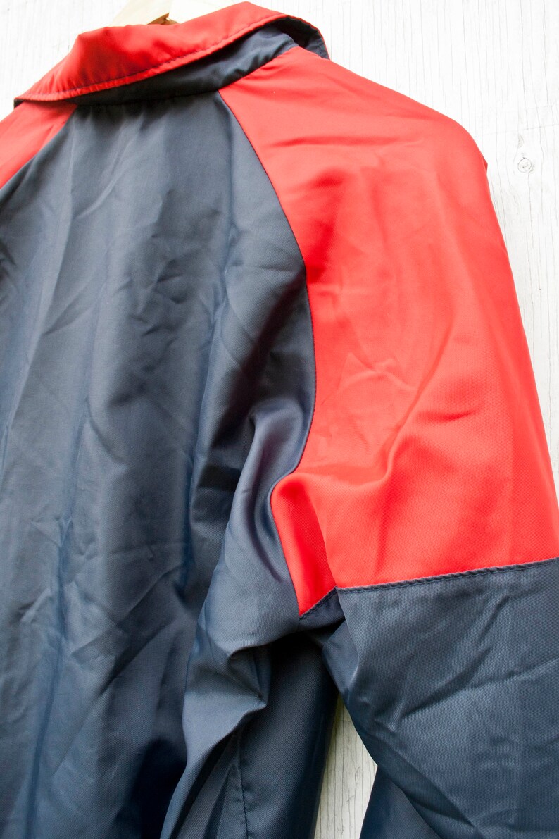 May include: A navy blue and red jacket with a zipper closure. The jacket has a red panel on the right side of the back and sleeves.
