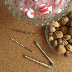 May include: A silver nutcracker with two prongs and a handle. Two silver nut picks are also pictured. A bowl of nuts and candies is in the background.