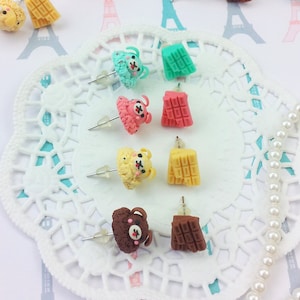 Könnte beinhalten: Ein Set mit 10 Paaren handgemachter Polymer Clay Ohrringe mit niedlichen Bärenköpfen und verschiedenen Schokoladenriegel-Designs. Die Ohrringe werden auf einer weißen Serviette mit einer Perlenkette präsentiert.