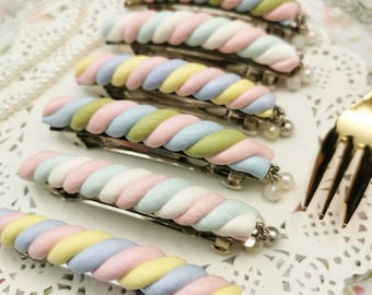 May include: Six pastel-colored twisted marshmallow hair clips with silver barrettes and pearl accents. The clips are arranged in a row on a white lace surface.