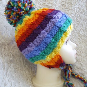 May include: A rainbow striped knitted hat with a colorful pom pom on top. The hat has a long tie that is also striped with rainbow colors.