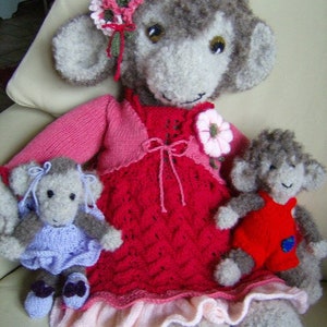 Puede incluir: Una muñeca de mono de punto gris que lleva un vestido rosa y rojo con una flor en el hombro y una muñeca de mono de punto gris más pequeña que lleva un vestido rojo.