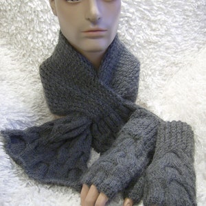 May include: A gray knitted scarf and fingerless gloves set. The scarf is folded and draped around a mannequin's neck. The gloves are laid out on a white fuzzy surface.