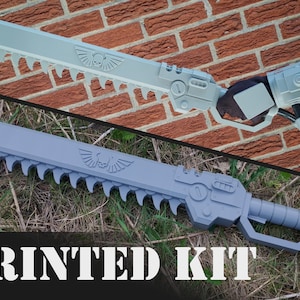 May include: A gray 3D printed model of a futuristic chainsaw with a skull and wings emblem. The text "PRINTED KIT" is visible at the bottom of the image.