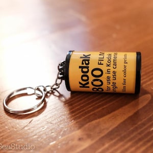 May include: A yellow and black keychain shaped like a roll of Kodak 800 film. The keychain has the text "Kodak 800 FILM" and "for use in Kodak single use cameras film for color prints".