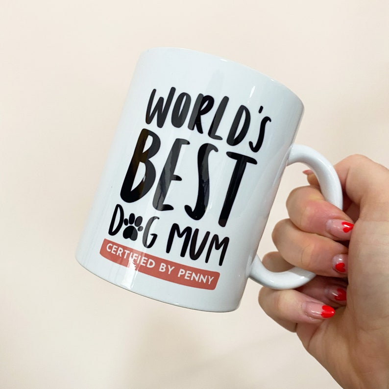 11oz ceramic mug personalised gift for dog lover and dog mum gift that reads "World's best dog mum certified by [chosen dog name here]" in black and white typography with an illustration of a dog paw