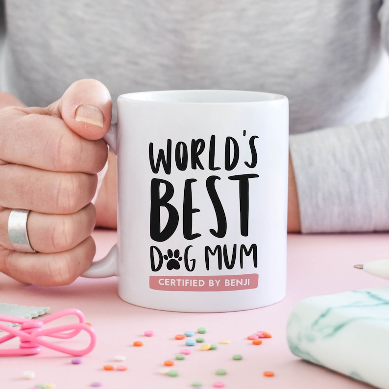 11oz ceramic mug personalised gift for dog lover and dog mum gift that reads "World's best dog mum certified by [chosen dog name here]" in black and white typography with an illustration of a dog paw