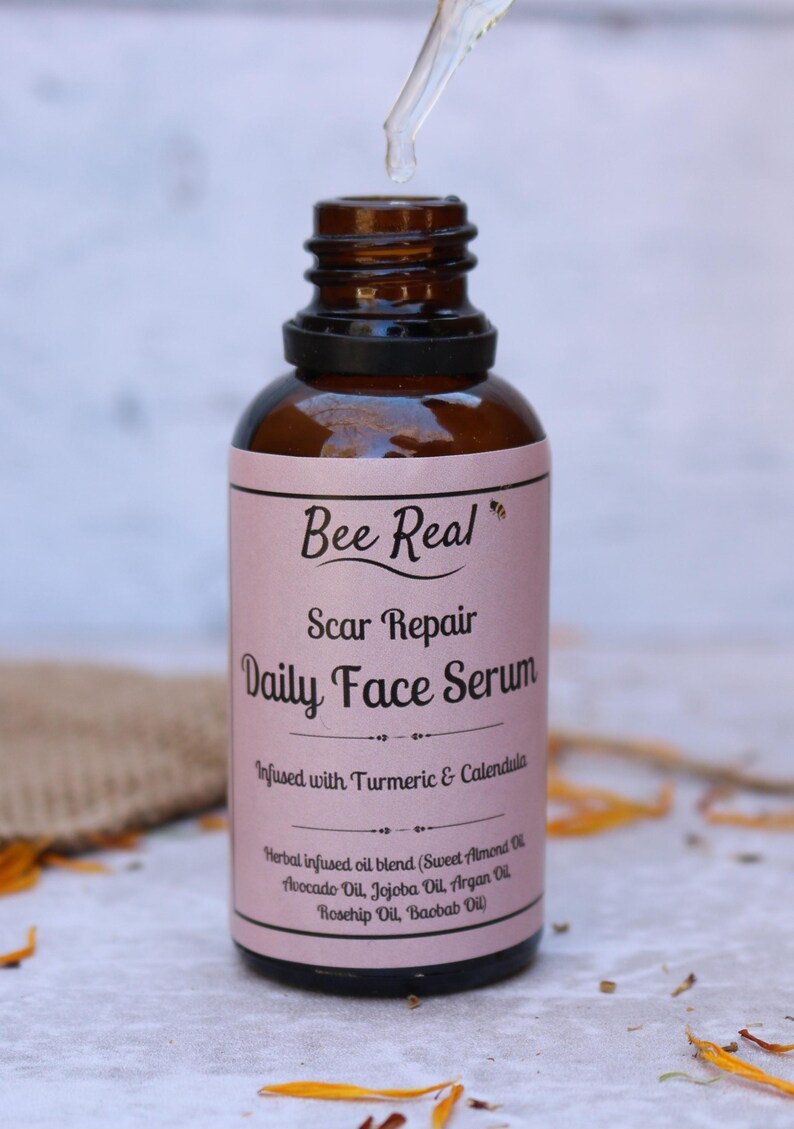 May include: A glass bottle with a dropper filled with a clear liquid. The bottle has a pink label with the text "Bee Real Scar Repair Daily Face Serum Infused with Turmeric & Calendula Herbal infused oil blend (Sweet Almond Oil, Avocado Oil, Jojoba Oil, Argan Oil, Rosehip Oil, Baobab Oil)"