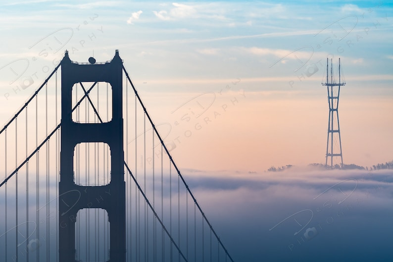 Puede incluir: Una silueta del puente Golden Gate con la torre de San Francisco en el fondo. El puente est&aacute; en primer plano y la torre est&aacute; en la distancia. Ambas estructuras son visibles contra un cielo brumoso, rosa y azul.