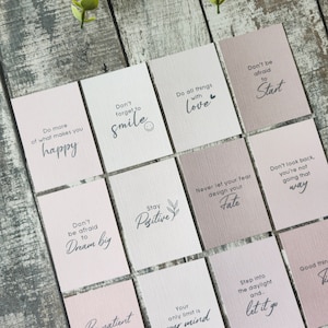 May include: A set of 10 pink and white cards with inspirational quotes printed on them. The quotes include "Do more of what makes you happy", "Don't forget to smile", "Do all things with love", "Don't be afraid to start", "Don't be afraid to dream big", "Be patient with yourself, nothing in nature blooms all year", "Stay positive", "Never let your fear design your fate", "Your only limit is your mind", "Step into the daylight and... let it go".