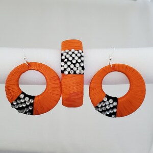 May include: A set of orange and black earrings and a matching bracelet. The earrings and bracelet are decorated with rhinestones.